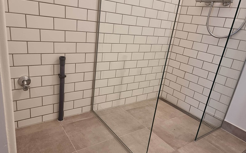 Brusekabine med fliser i forskellige farver og gråt armatur.