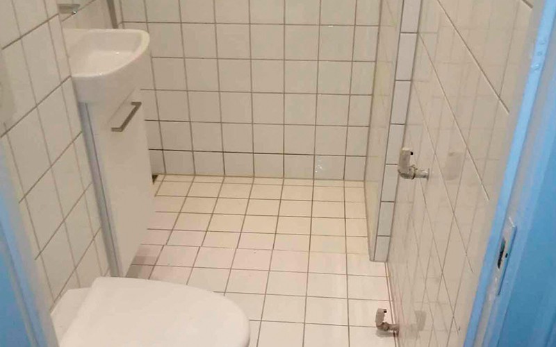 Fliser og dørkarm i forskellige farver på simpelt badeværelse.